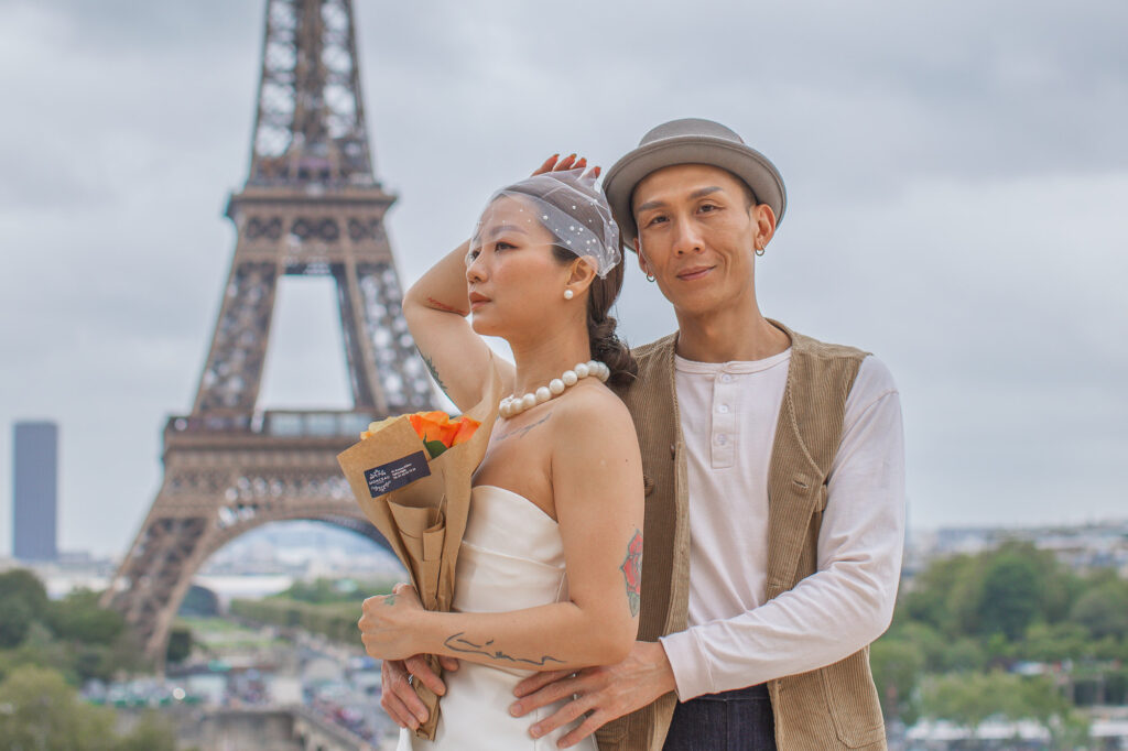 Newlyweds posing in front of the Eiffel Tower with a bouquet of orange roses. Radina Dianova - Paris based photographer