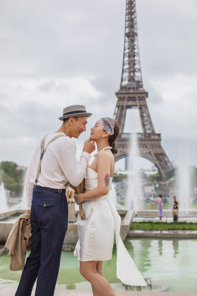 A playful moment between newly eloped bride and groom in front of the Eiffel Tower. The groom is holding the chin of the bride. Radina Dianova - Paris based photographer