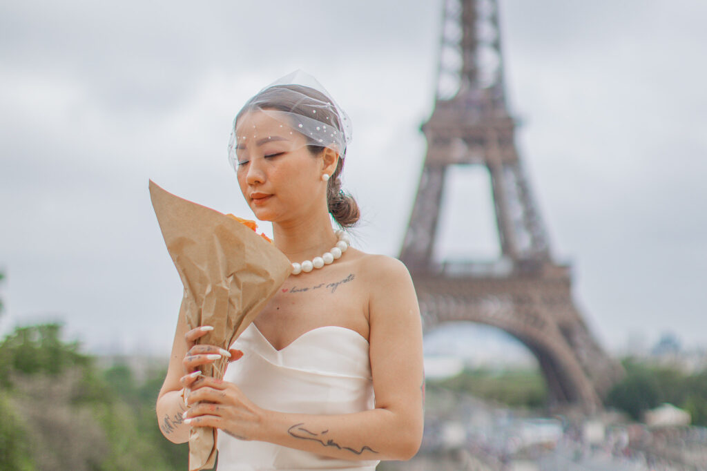 A bride smells her bouquet of orange roses in front of the Eiffel Tower. Radina Dianova - Paris based photographer