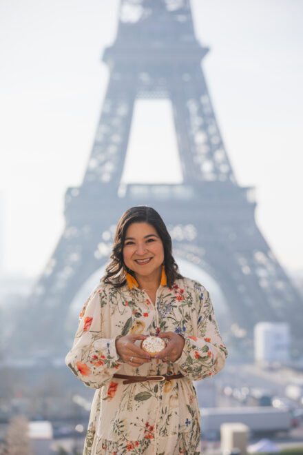 Woman holds a small cake in front of the Eiffel Tower