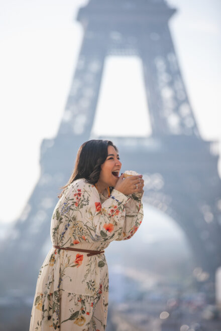 Woman eating a small cake in front of the Eiffel Tower