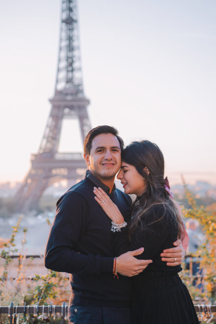 A young couple is embracing in front of the Eiffel Tower basking in the soft sunrise light