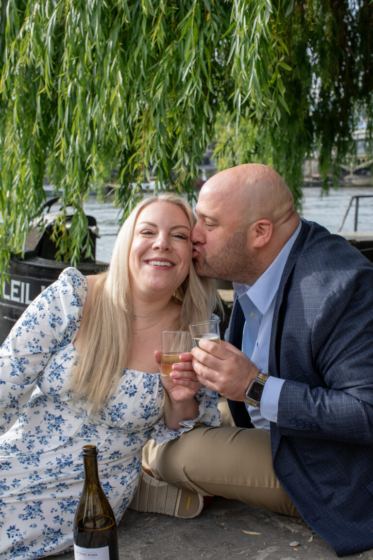 Dan kisses Katie in front of a willow tree by the Seine river, as they toast for their engagement