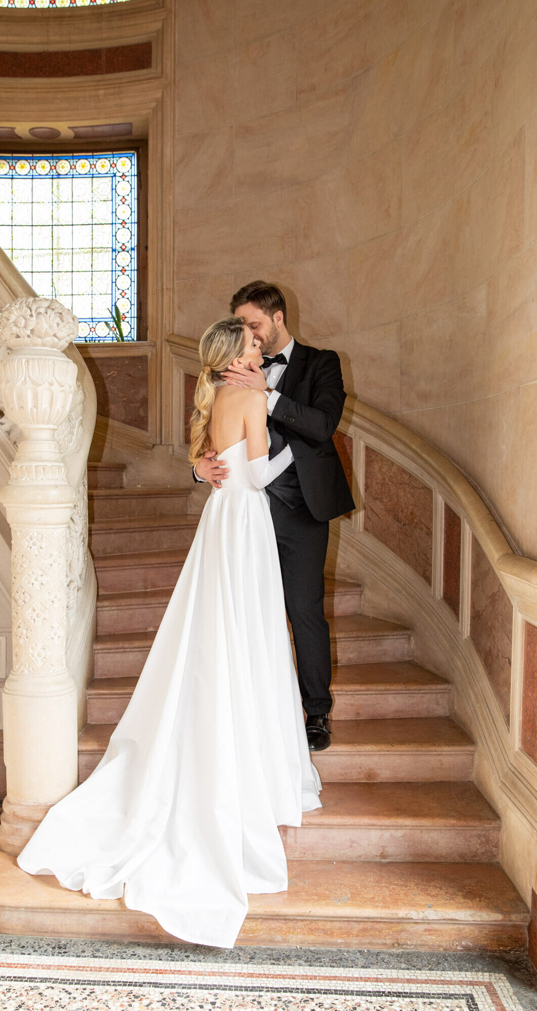 Bride and groom kissing on elegant château staircase during Burgundy wedding portrait session